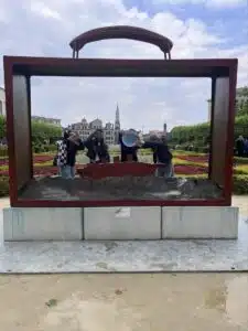 Scholieren poseren bij een groot kunstwerk van een koffer, terwijl ze het logo van 'Deze school duikt in taal' omhoog houden, promotie van meertaligheid.