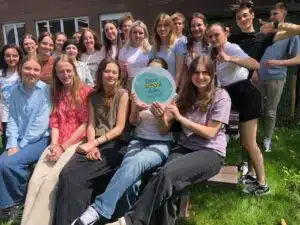 Groepsfoto van leerlingen in een tuin, met het 'Deze school duikt in taal' logo in het midden