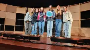 Groep studenten op podium houdt bord vast, viert taaldiversiteit met Duik in Taal campagne.