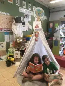 Twee leerlingen van GO Leefschool Het Biezebos lezen boeken onder een tipi met het logo "Deze school duikt in taal"