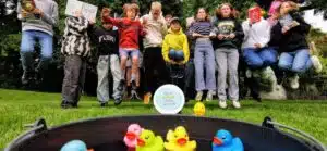 Leerlingen van ZOOM Freinet Kortrijk springen achter een badje met badeendjes heen met tussen hen in het logo "Deze school duikt in taal"